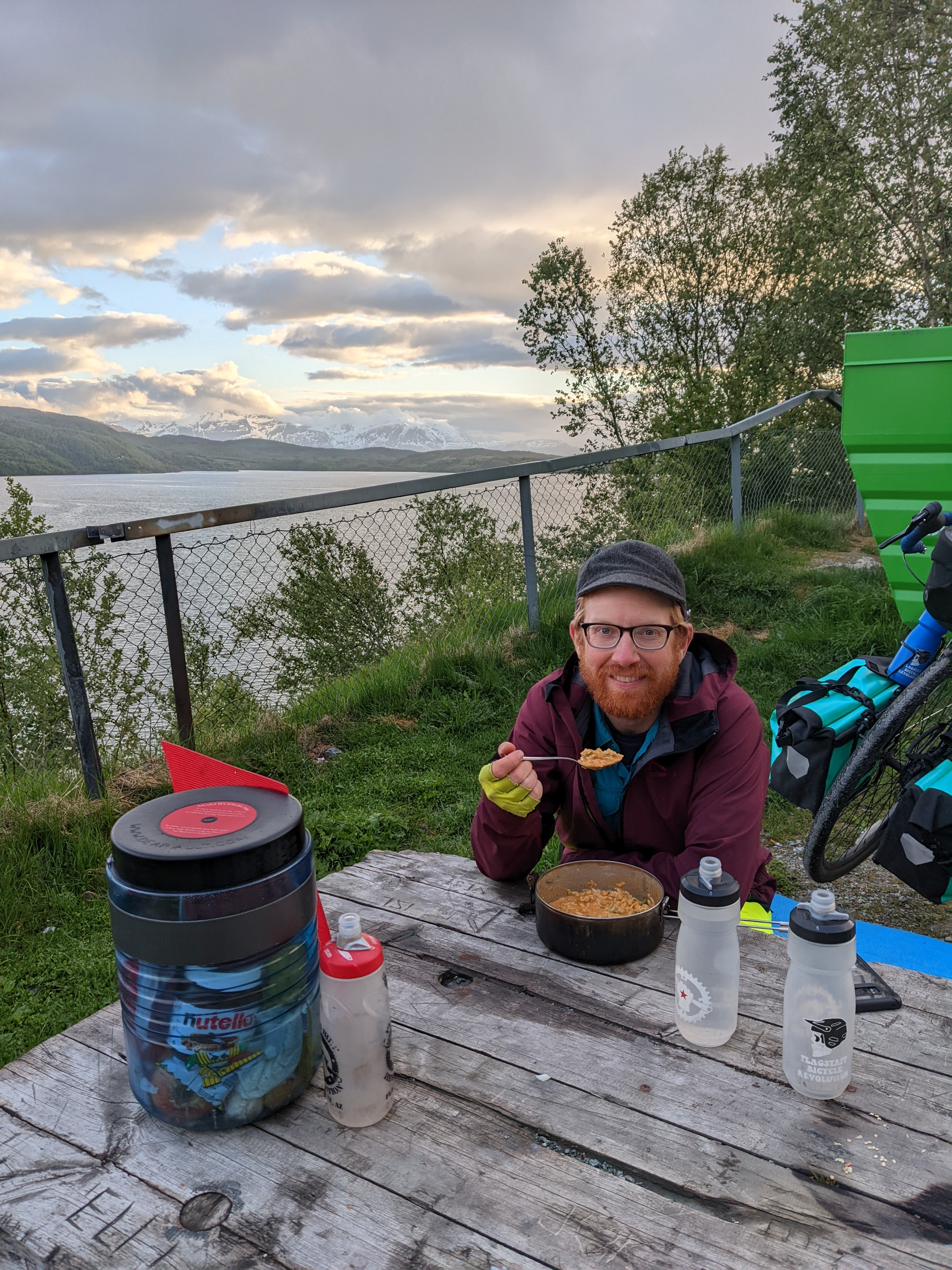 Chris eating dinner at a picnic table overlooking the fjord