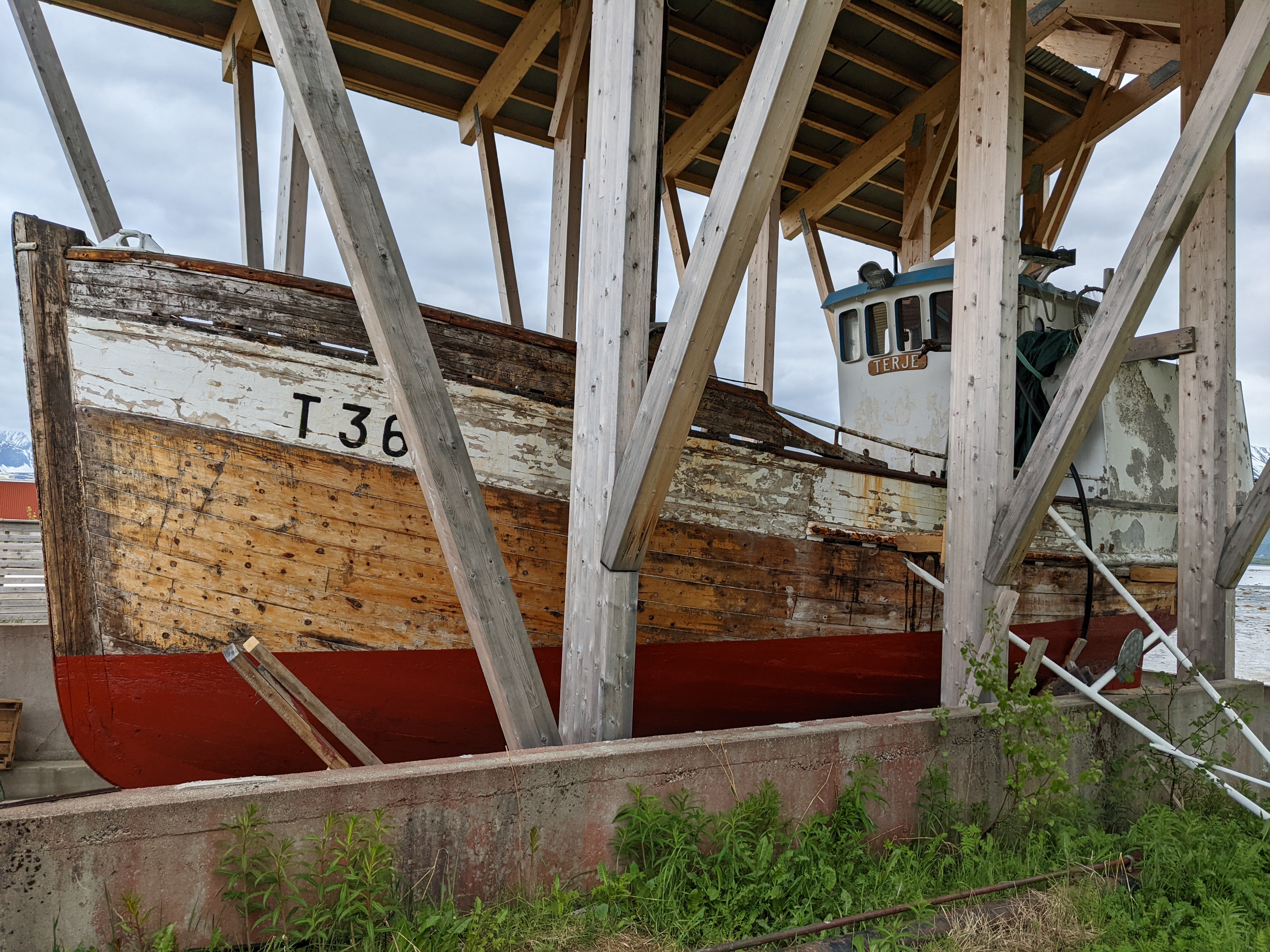 a large wooden boat with a cabin and a motor under a museum shelter