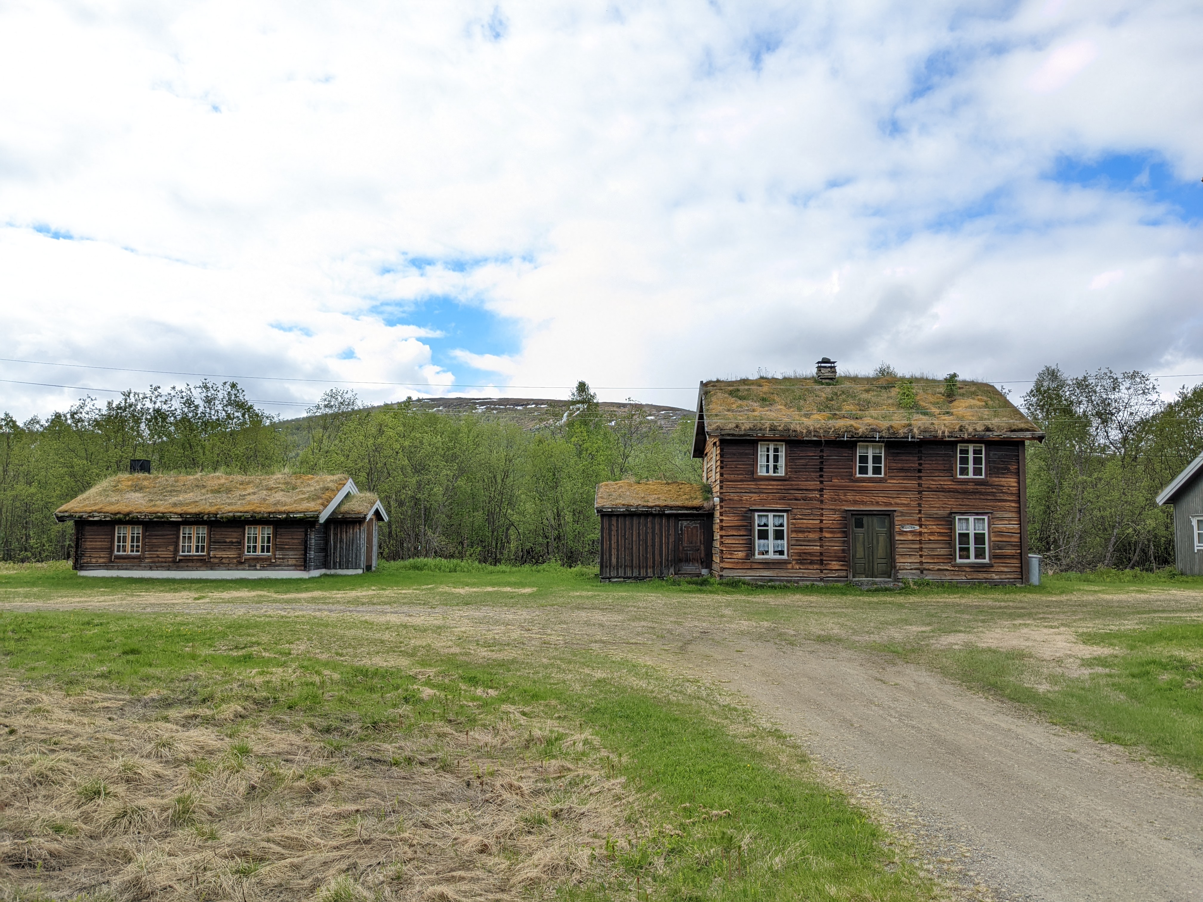 two old square-cut log cabins, one larger and one smaller, with sod rooves