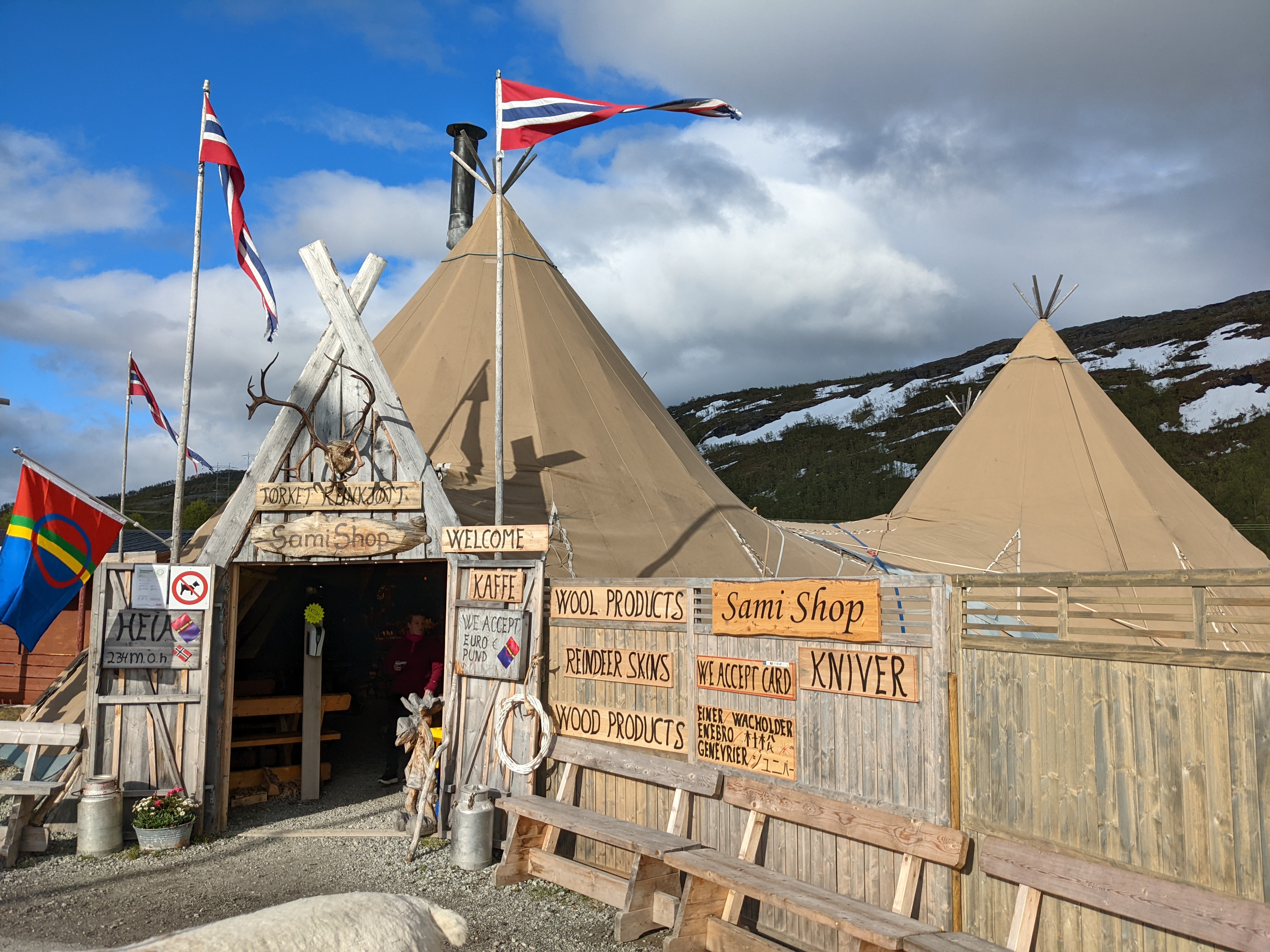 a view of the entrance to the sami shop tents with sami and norwegian flags flying and reindeer antlers above the door