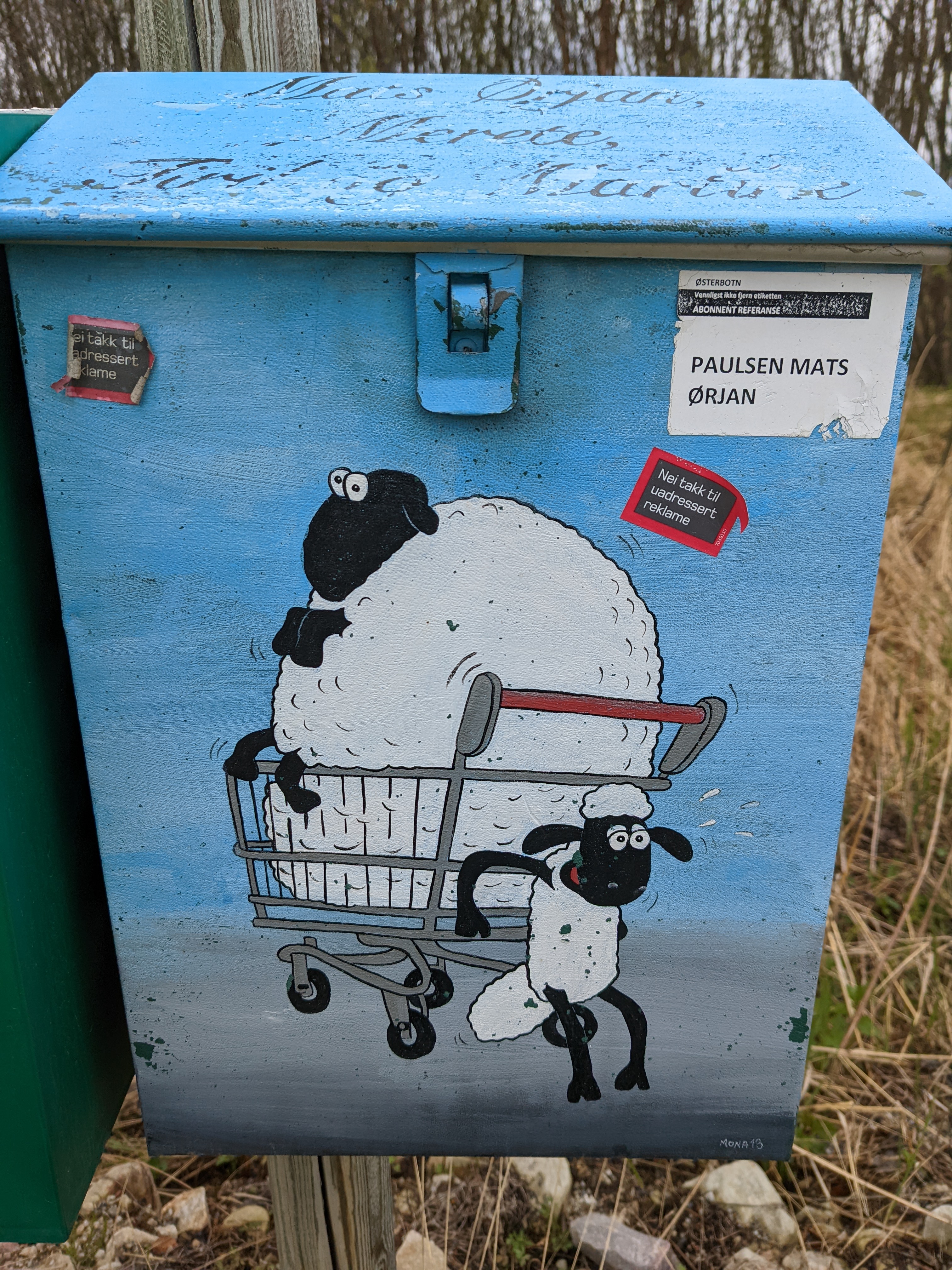 A mailbox with a picture of a lamb pushing a fat ewe in a shopping cart