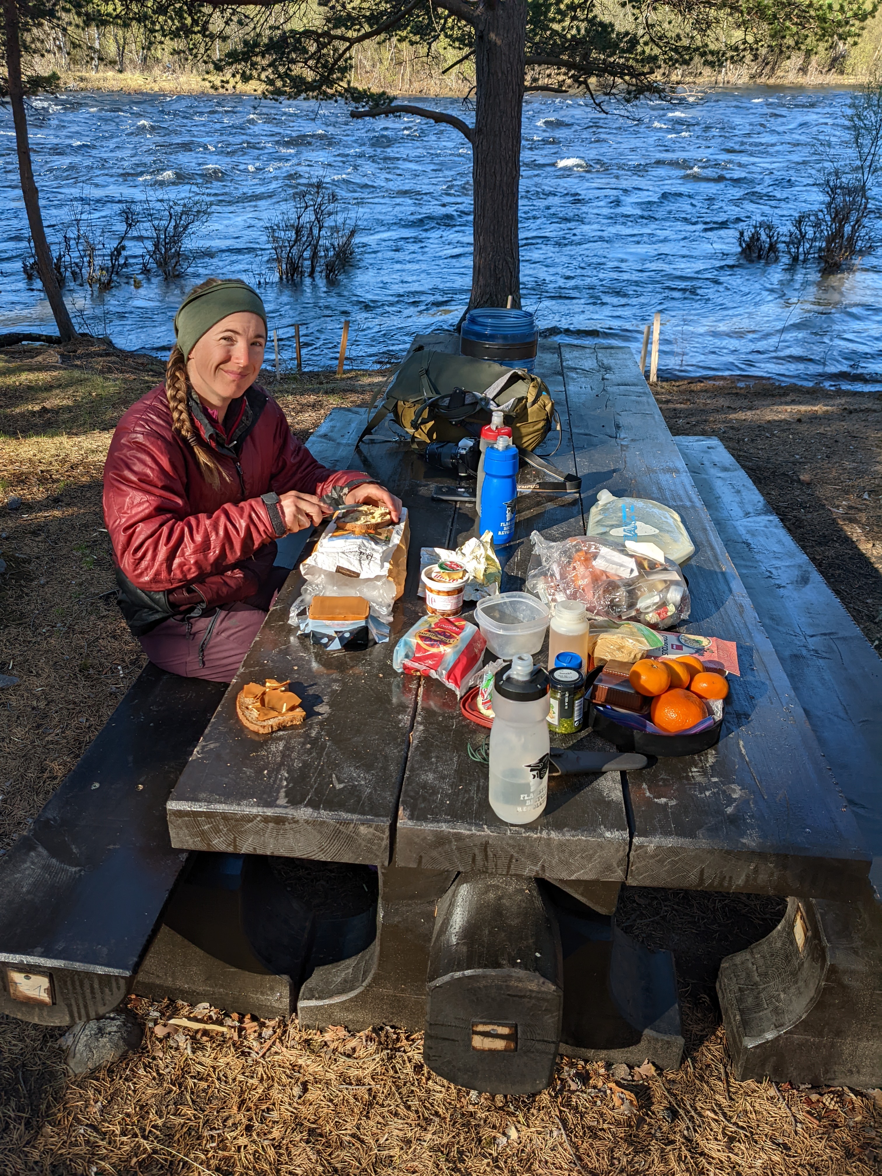 H spreading butter on bread at a picnic table by the water