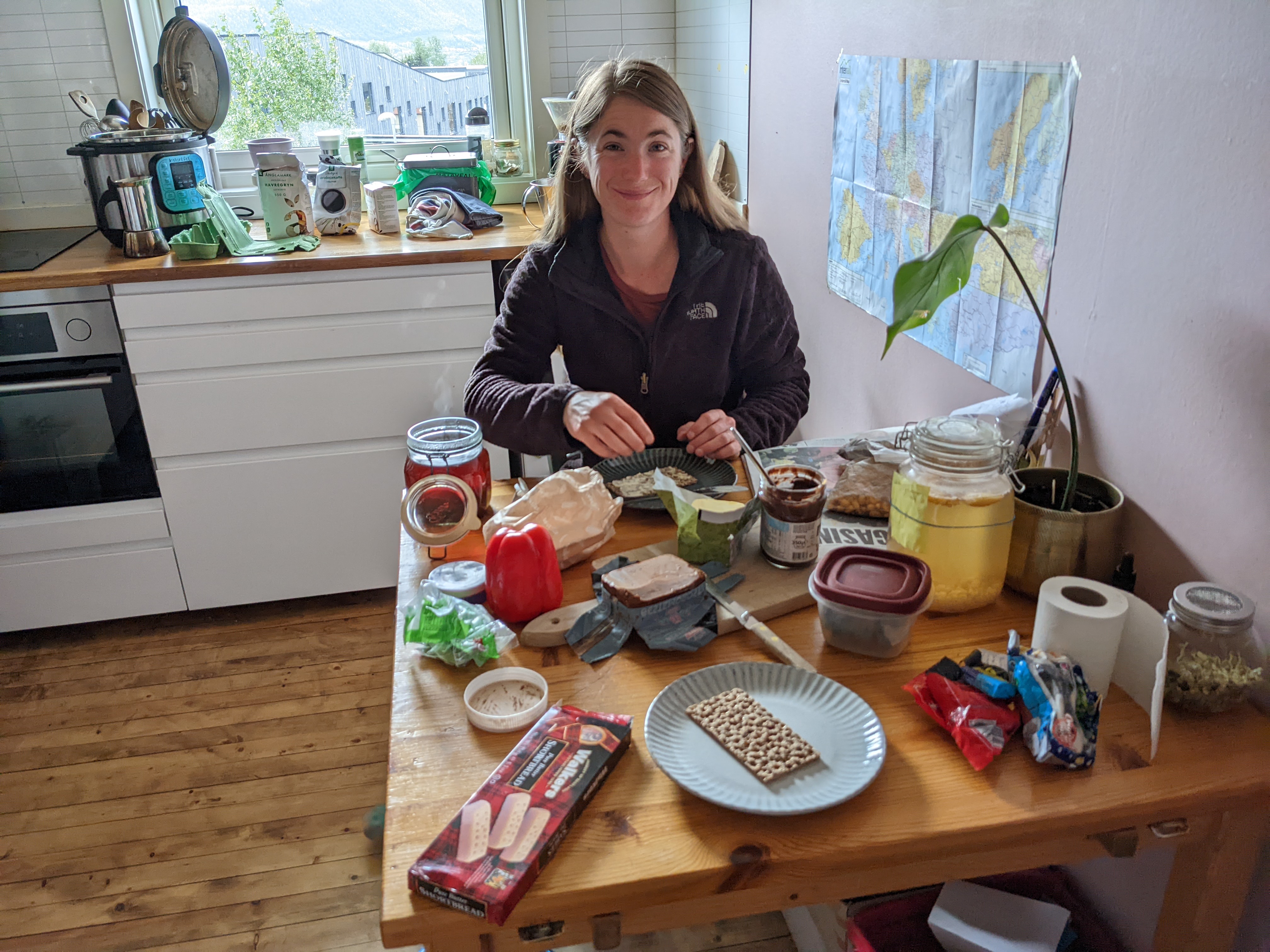 H sitting at a wooden table covered with breakfast foods in a bright wooden kitchen