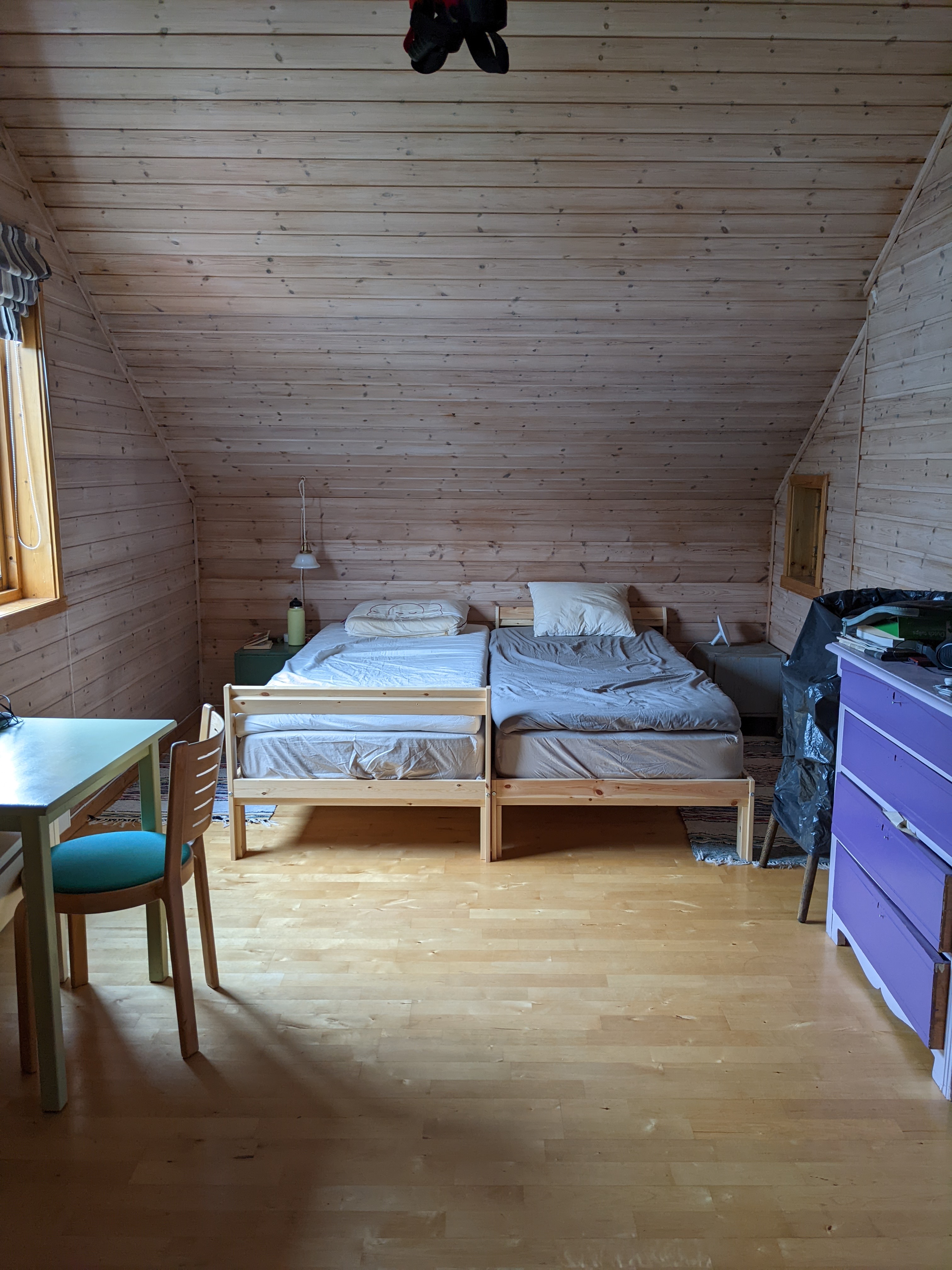 a tidy room with wooden floor, walls, and ceiling, and two adjacent twin beds