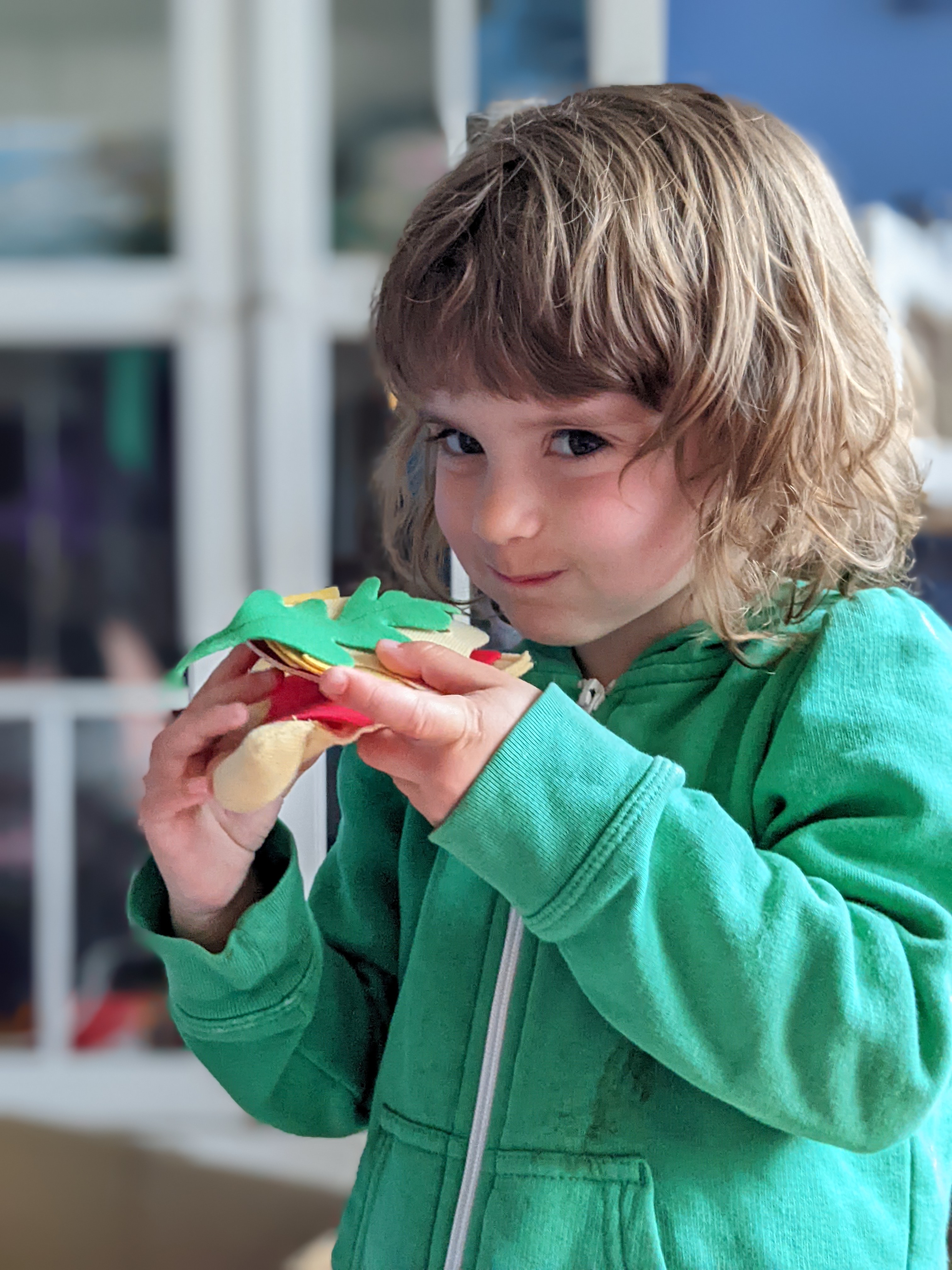 a young girl pretends to eat a slice of pizza made from felt ingredients