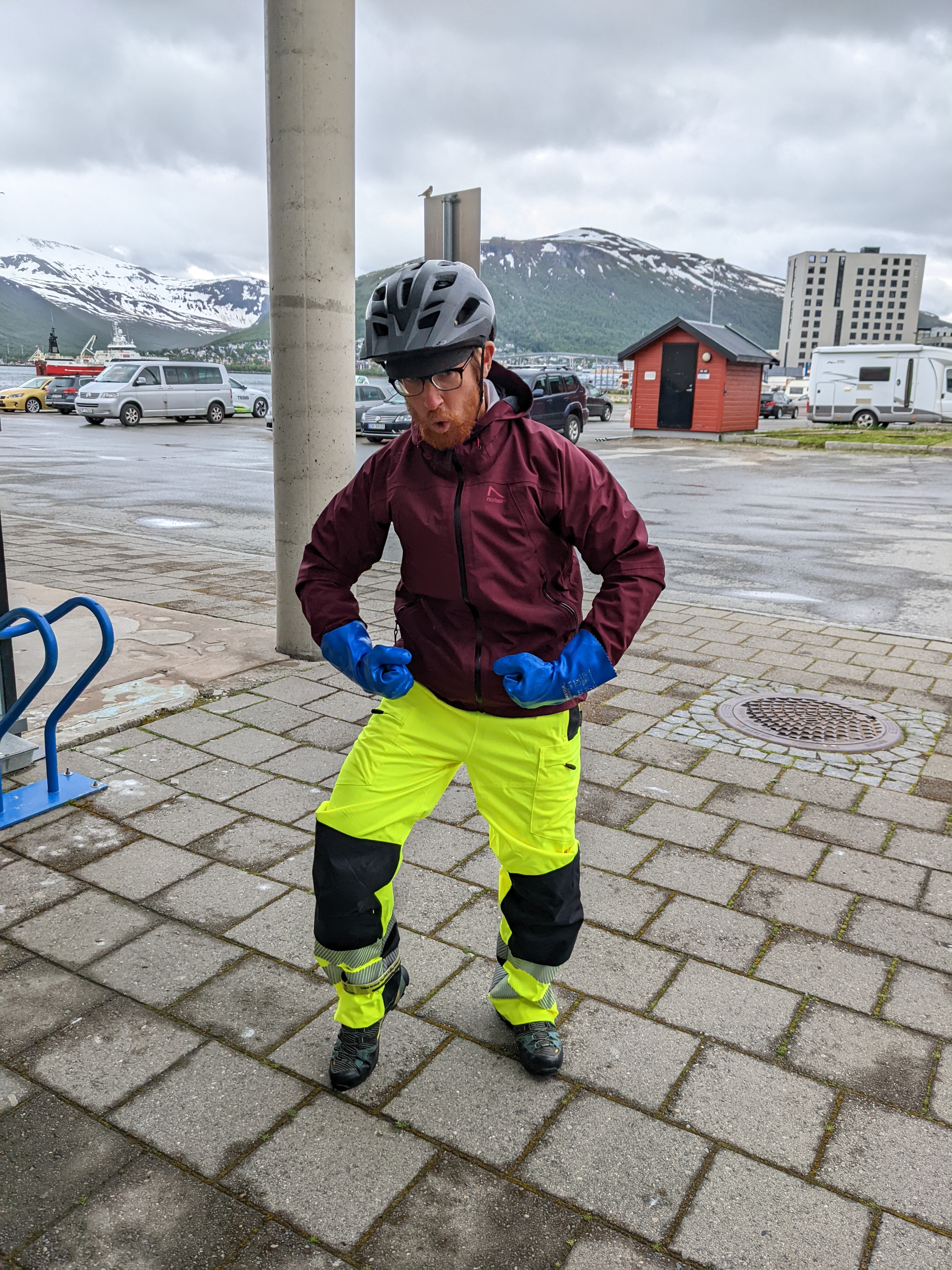 Chris flexing his muscles in neon yellow reflective rain pants, rain jacket, and blue rubber gloves