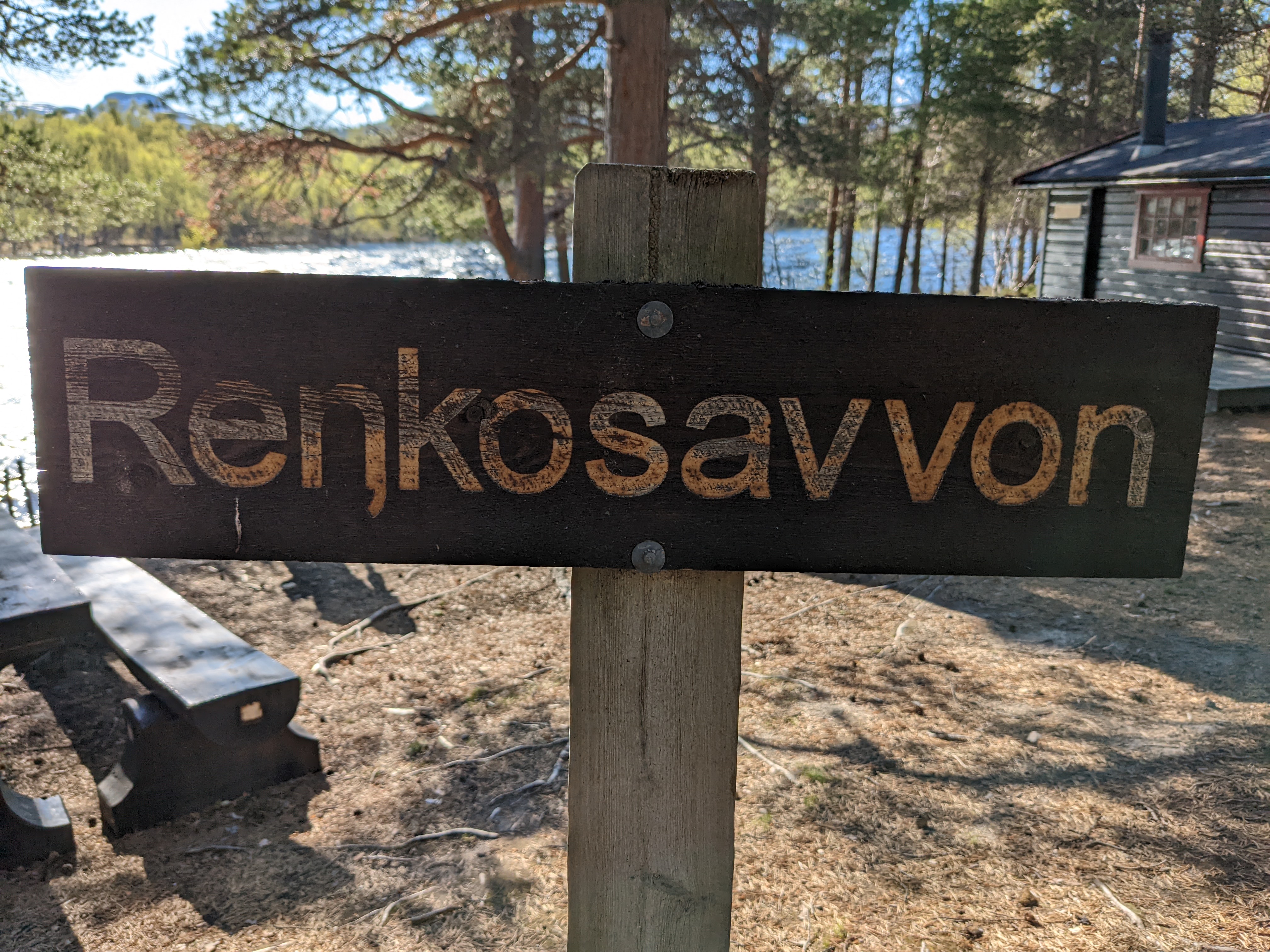 the cabin site's name in Sami on a sign, in front of the picnic table and river