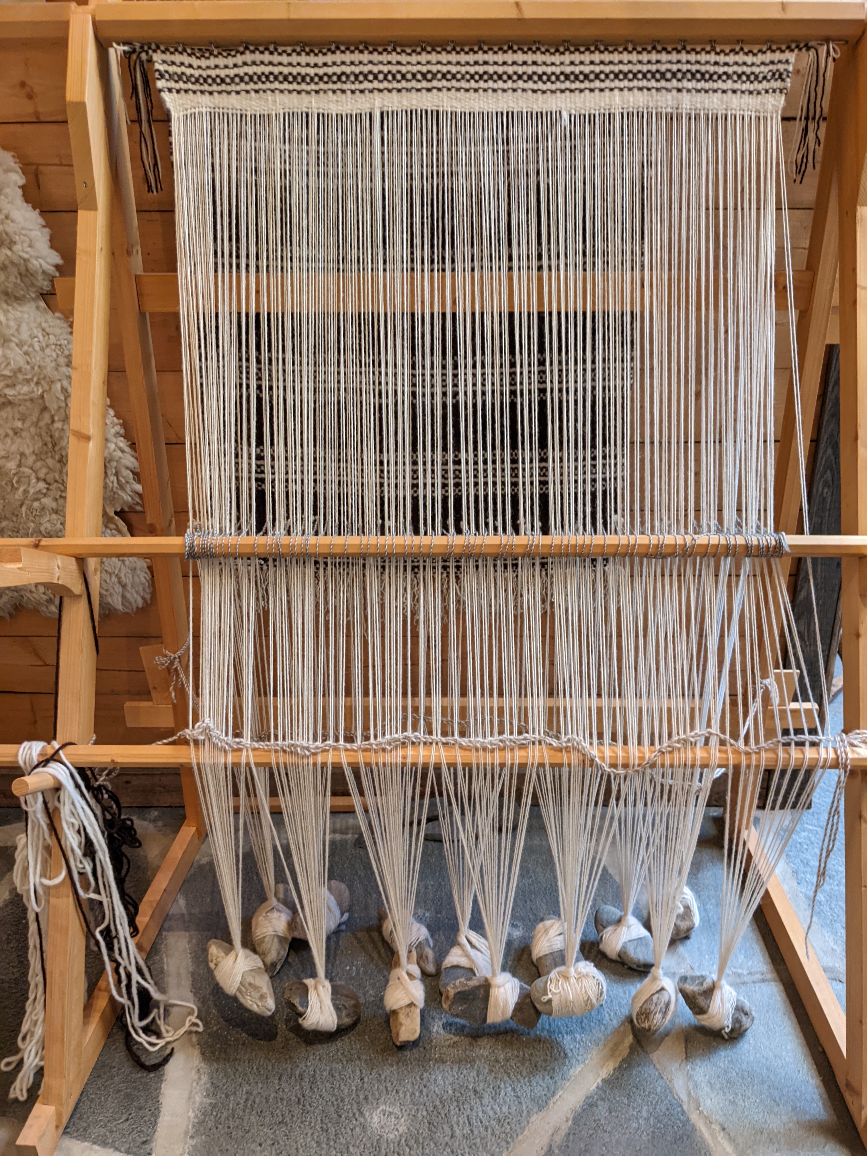 a neat wooden loom where the warp strands are held taught by hanging rocks