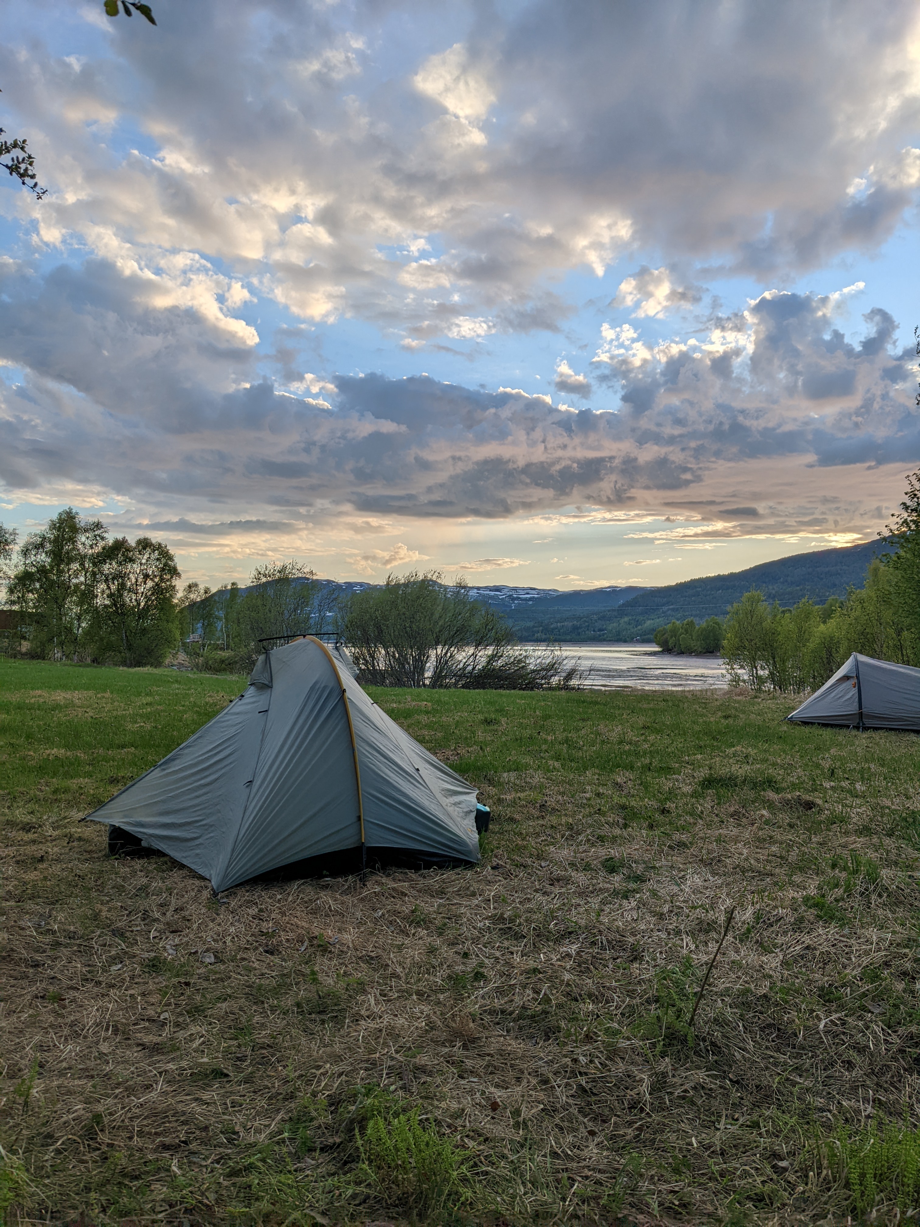 two tents at the edge of a field where the river meets the fjord