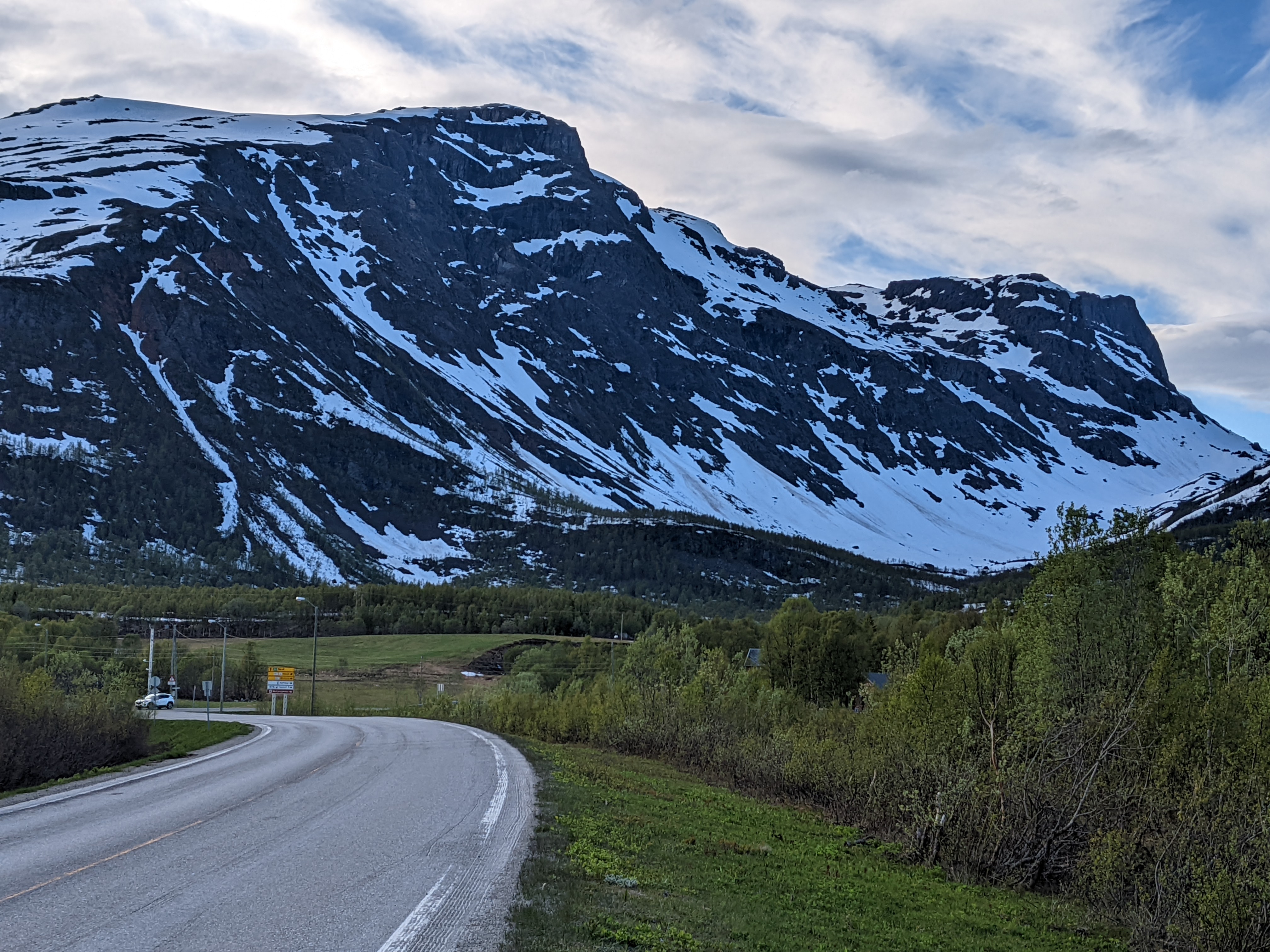 A dark stone and snow cliff fills the frame left of the road