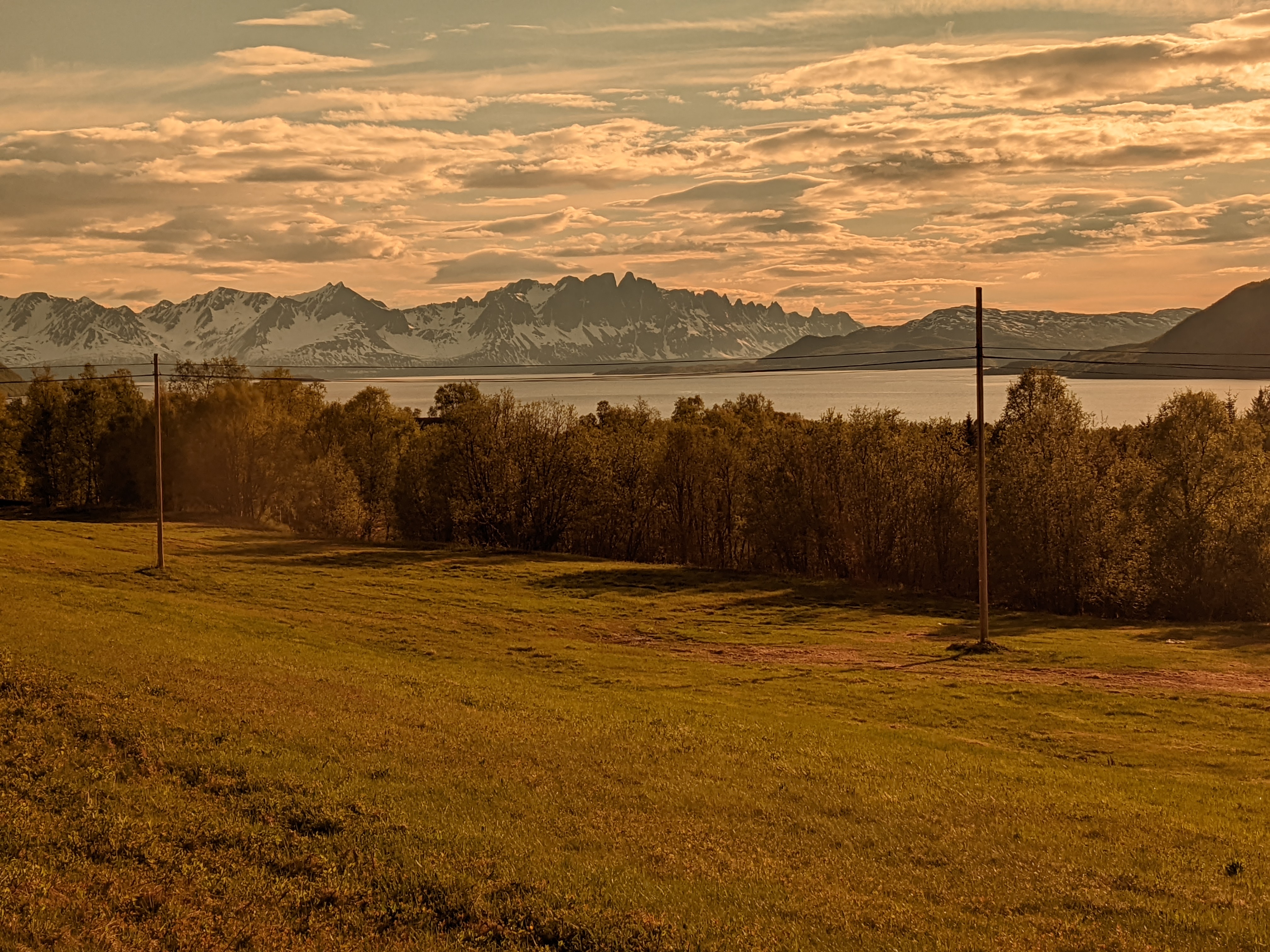 view of field, fjord, then mountains tinted orange by sunglasses