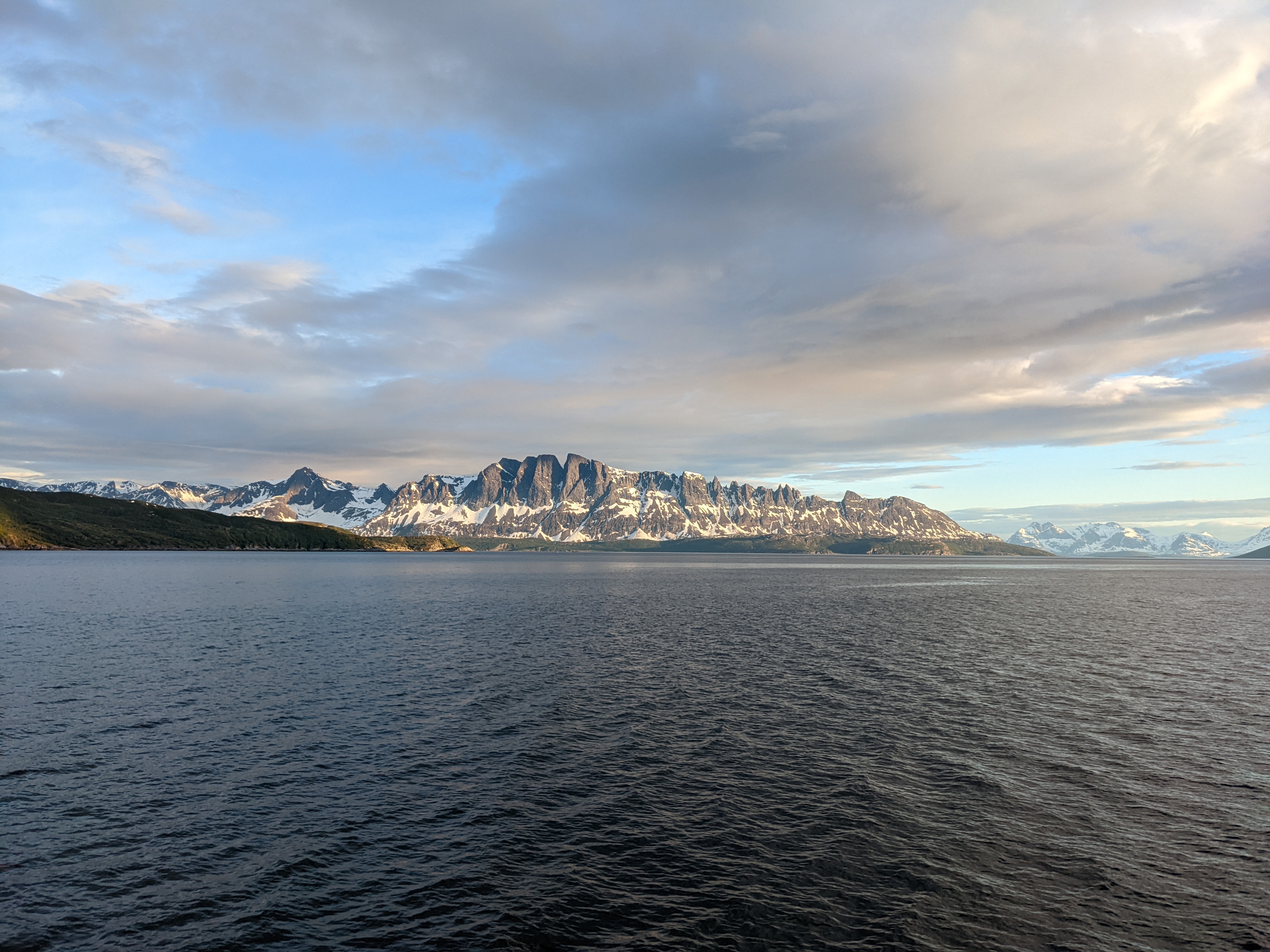 sharp rock spires above the water, with a distant set of snowcovered peaks at right