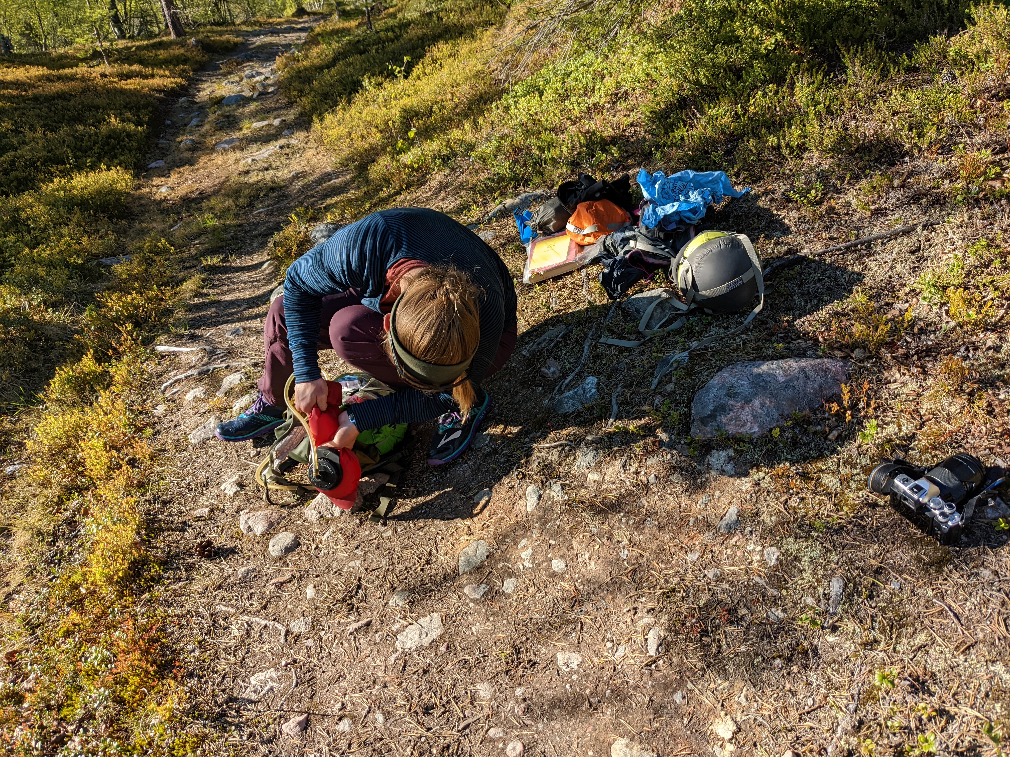 H crouched over a water bladder with the contents of her pack strewn behind her