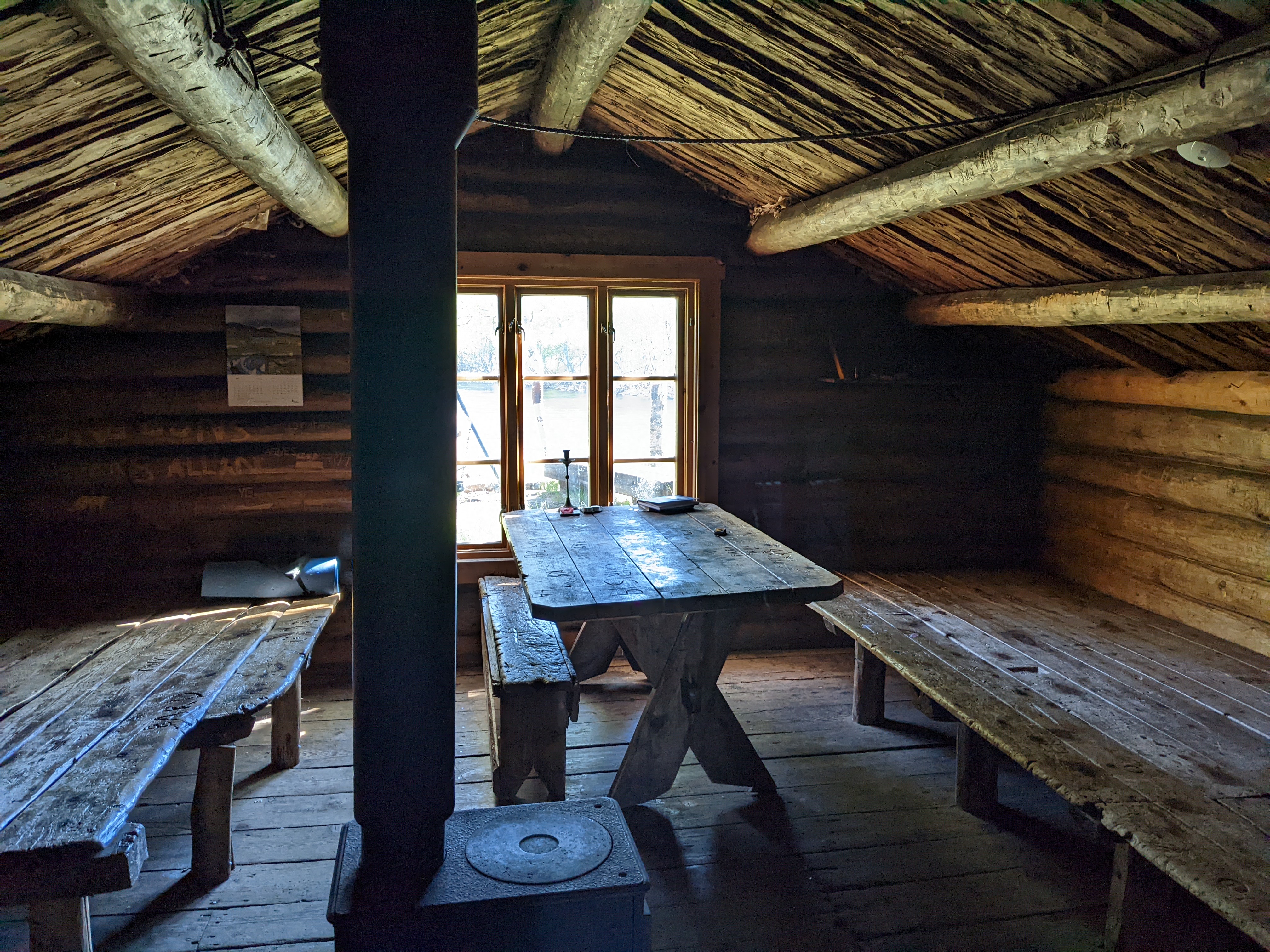 the inside of a wooden cabin with a woodstove and wooden tables and benches/sleeping platforms