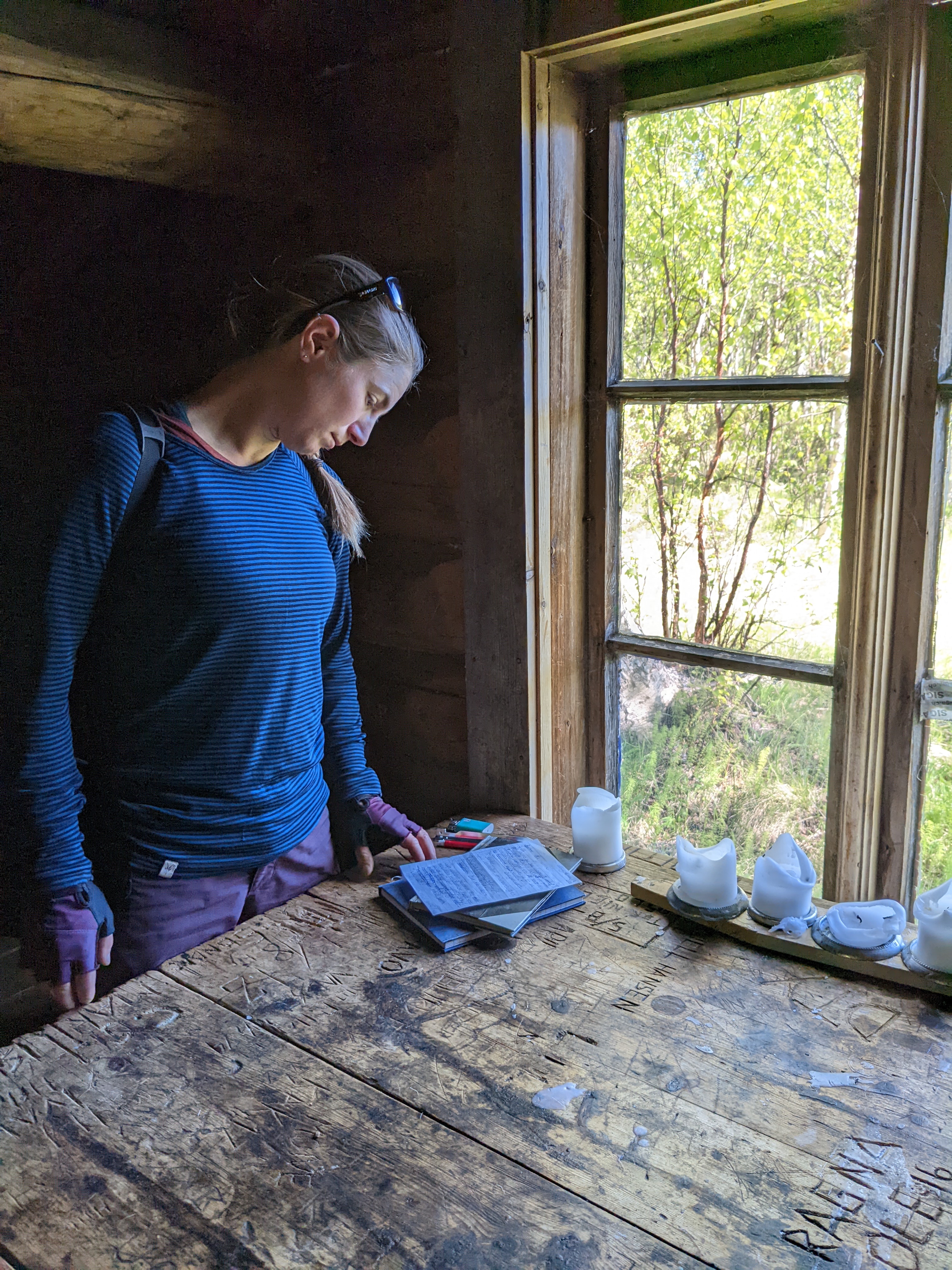 H reading some papers on a well-used wooden table in a cabin