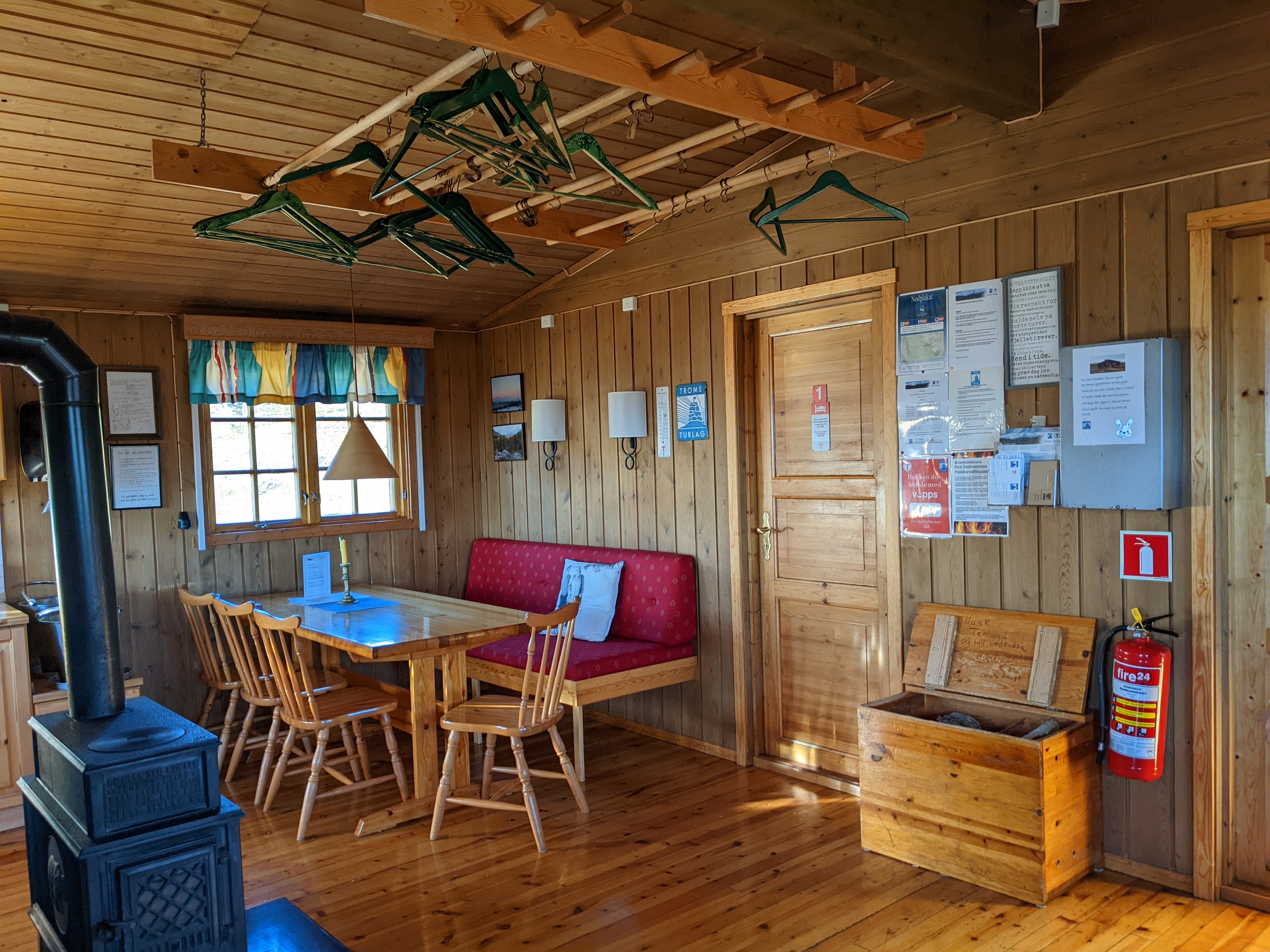 the bright, new interior of a DNT cabin with a woodstove, drying lines, and a kitchen table in the sunlight