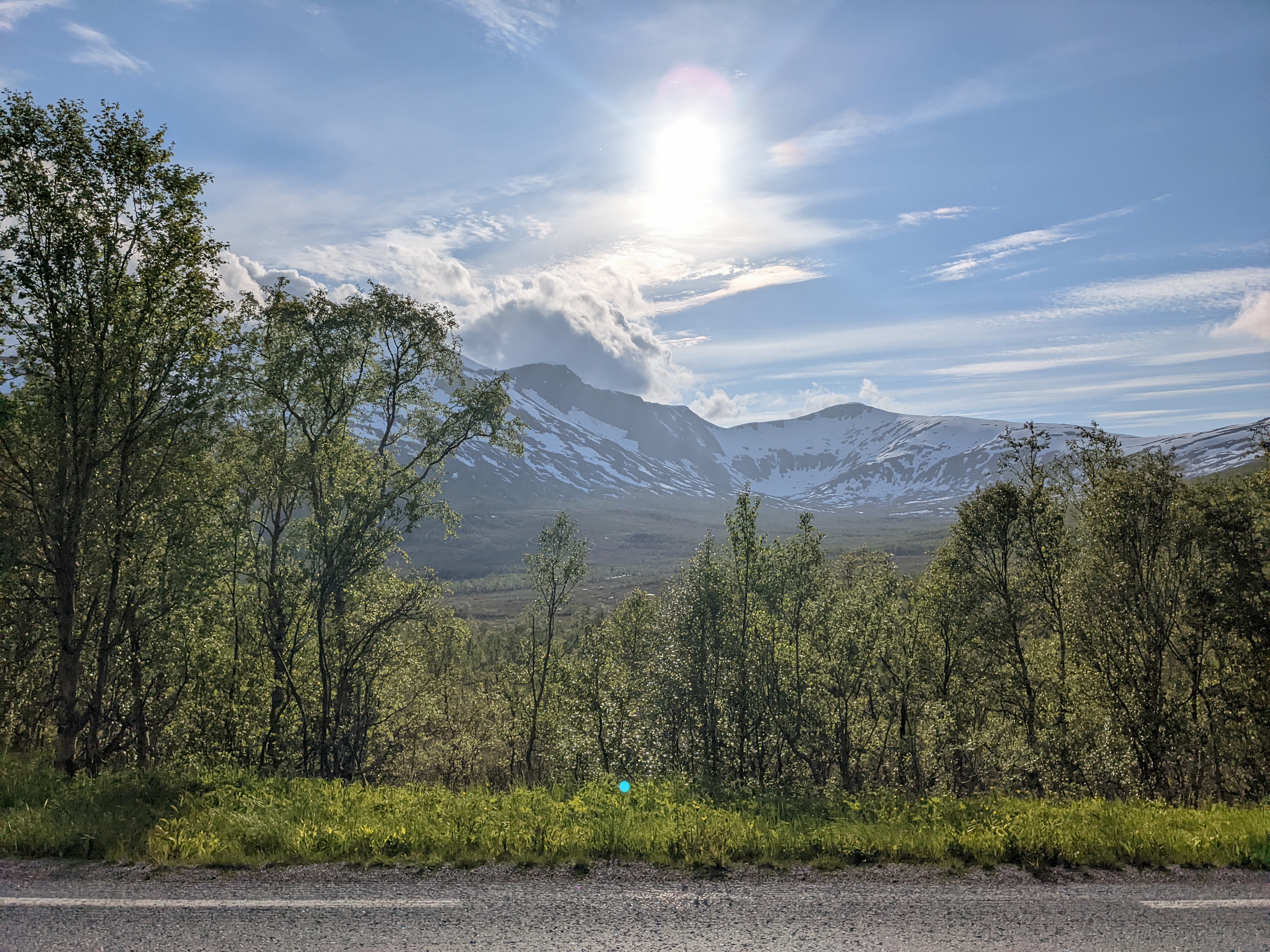 bright light in a blue sky with poofy dark clouds above mountains and marsh