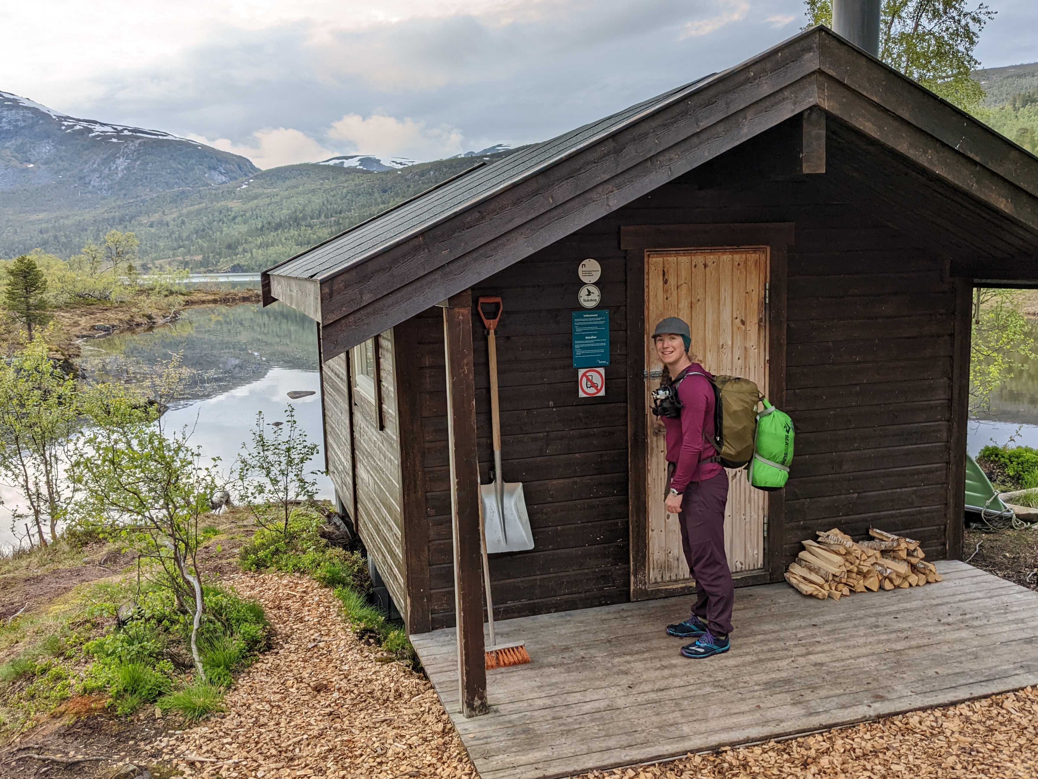 H opening the door to a small brown cabin on a lake