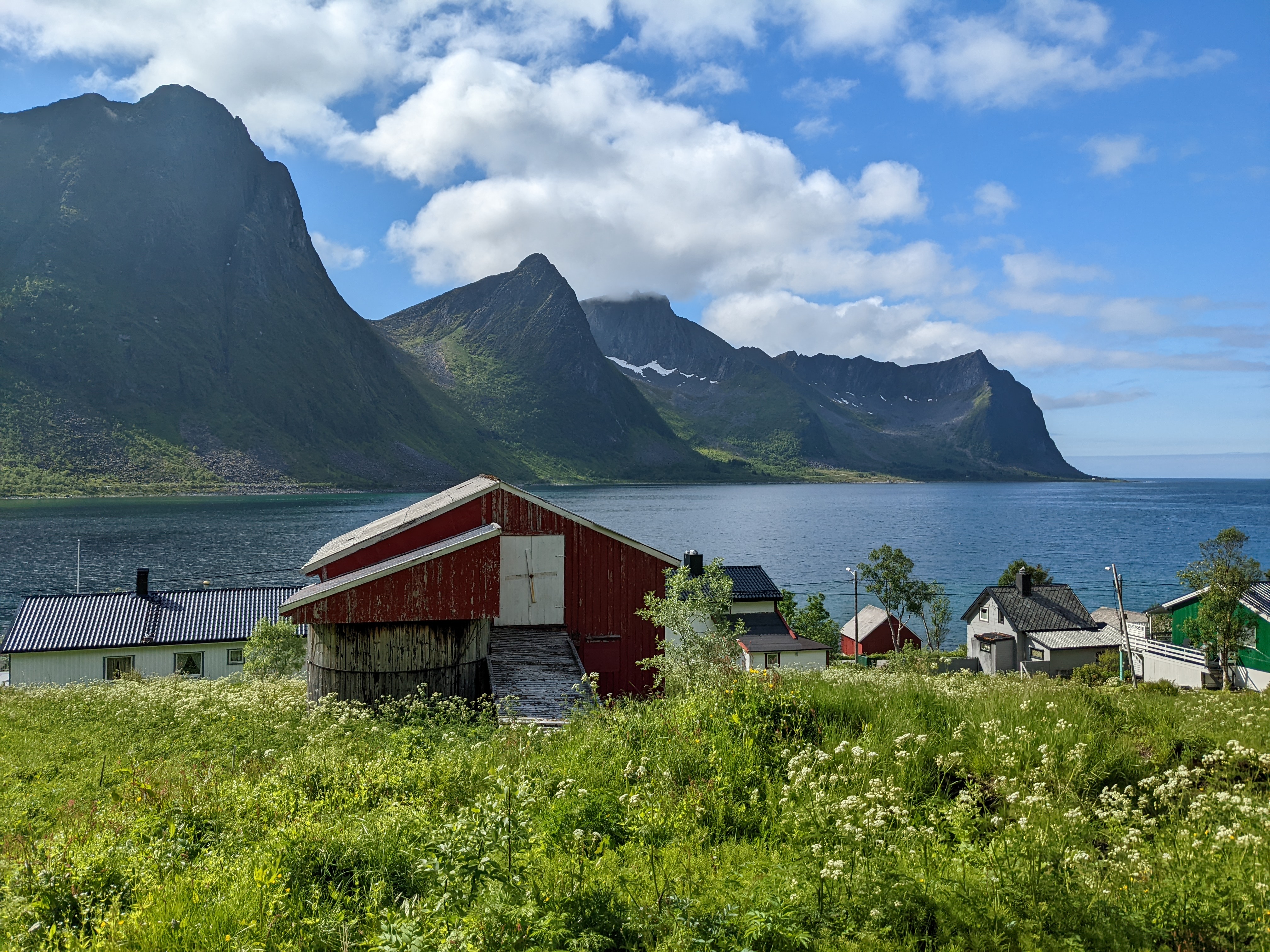 a red barn and some homes above the fjord, backed by bautiful mountains