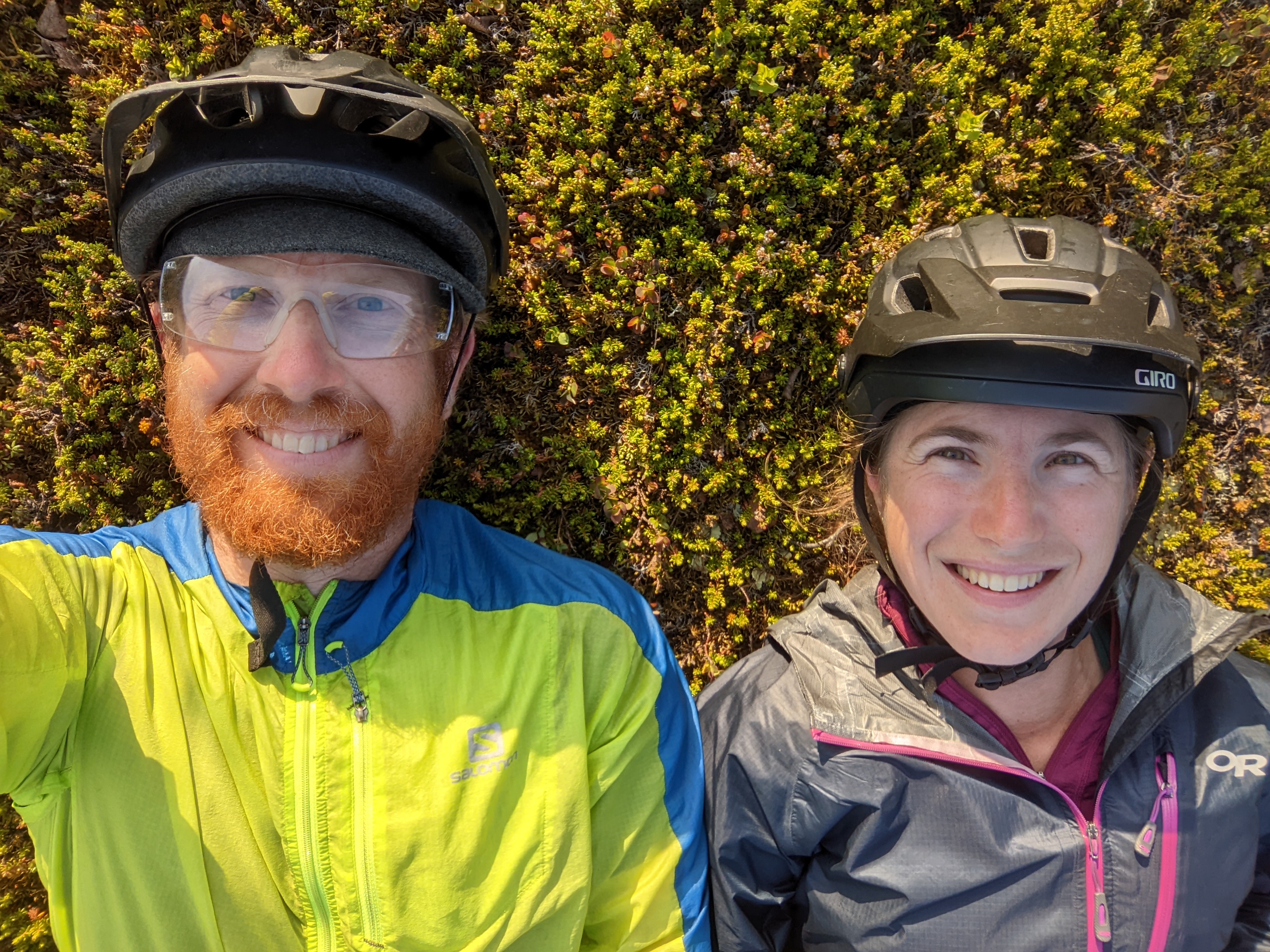 C and H laying side by side on crowberry meadow, shot from above. bike helmets still on