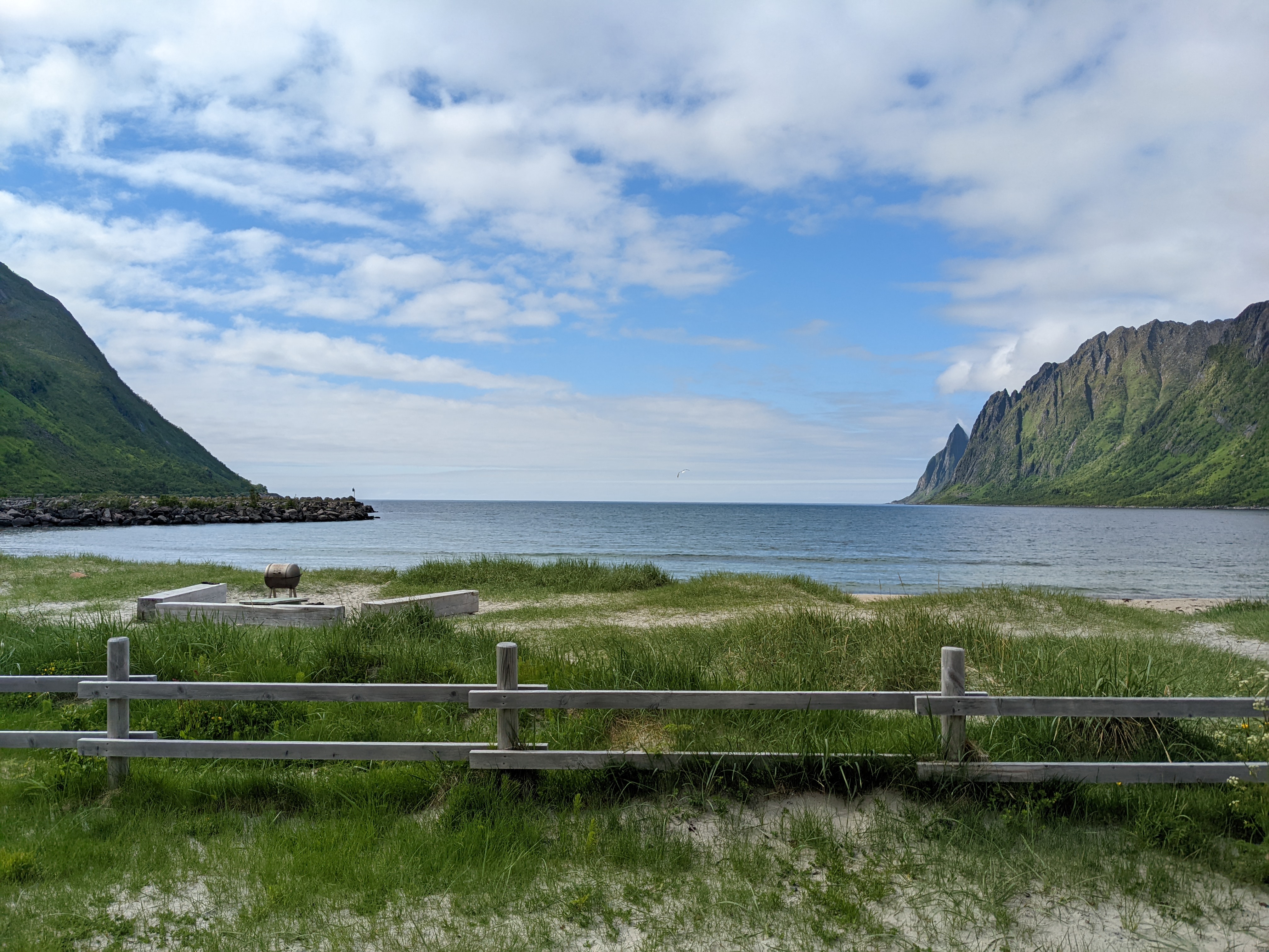 a white-sand beach with barbecue and benches and grass on the dunes