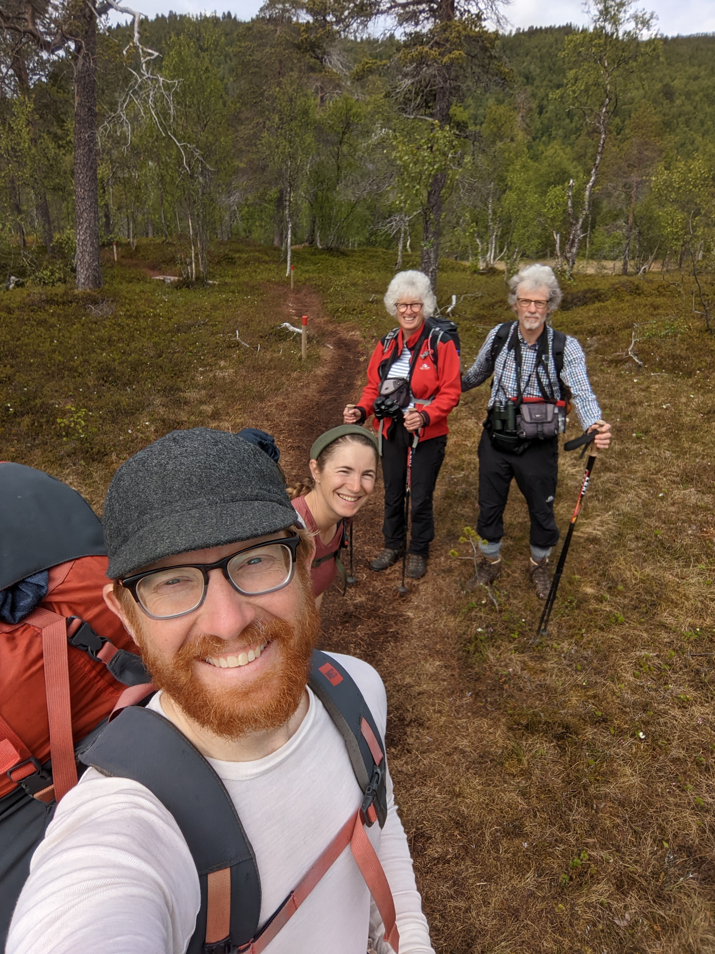 Selfie of Chris, H, and two white-haired hikers with trekking poles and binoculars