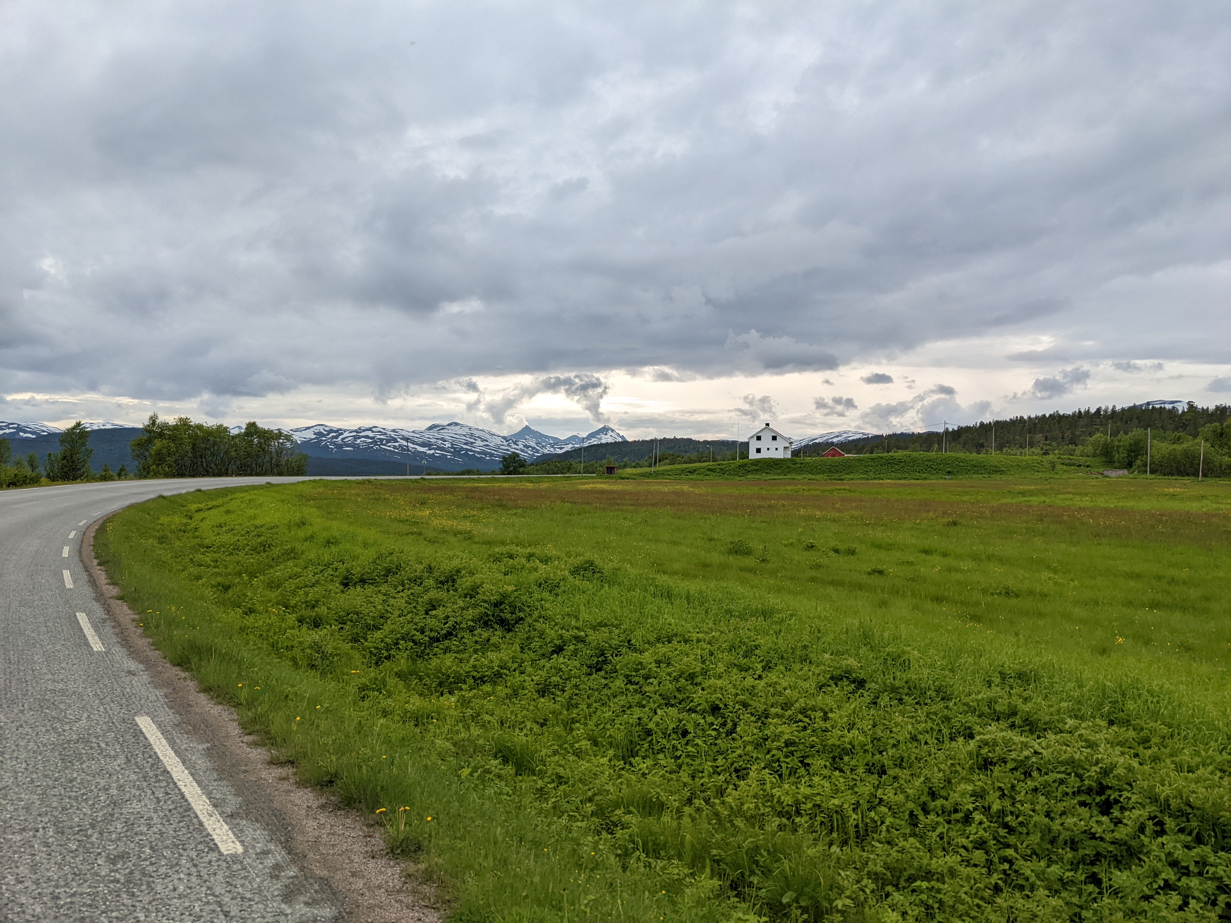 snowy peaks behind a meadow foreground, with a white farmhouse on a hill in the midground