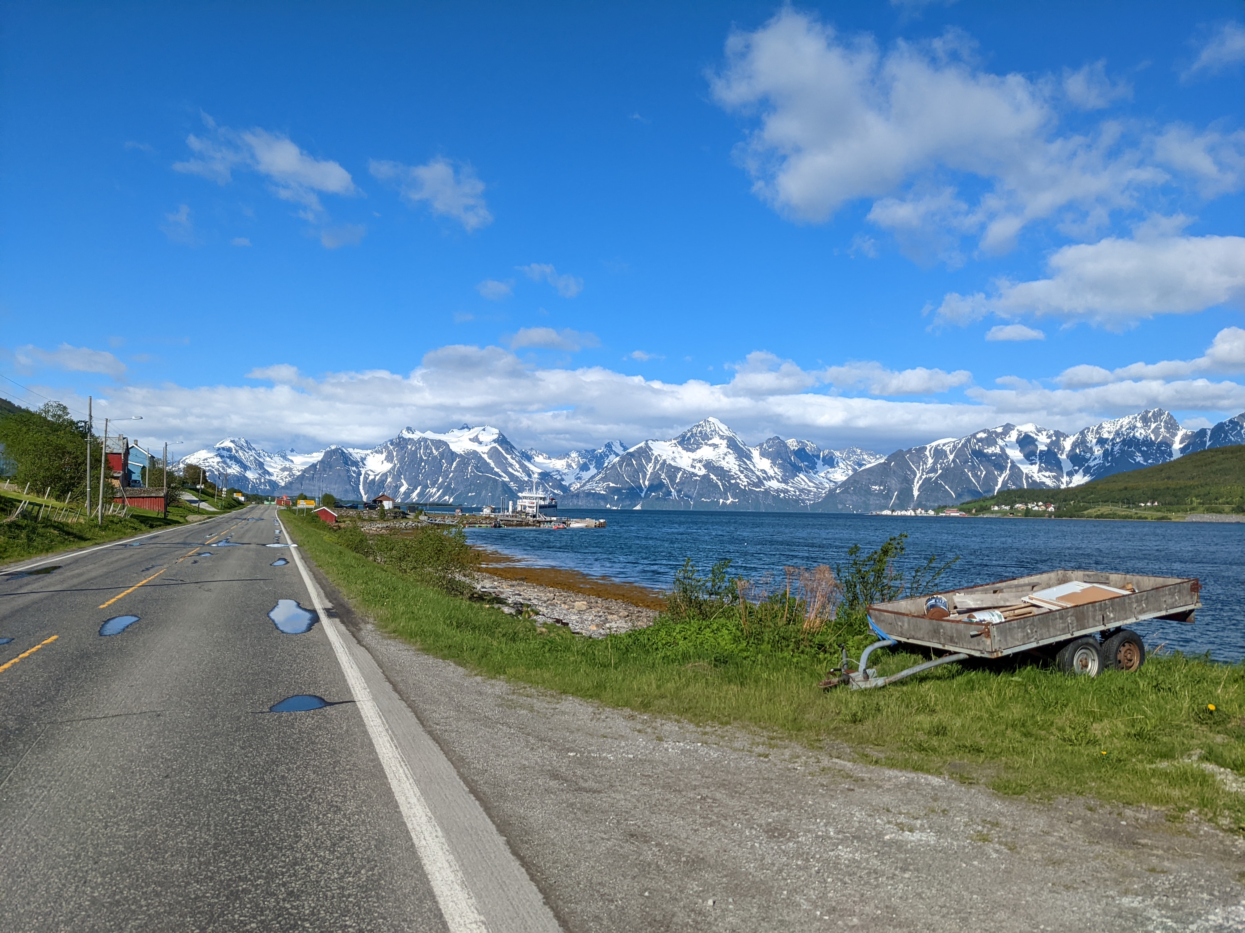 fjord coast with trailer by the road, boat in the water, and high peaks in the background