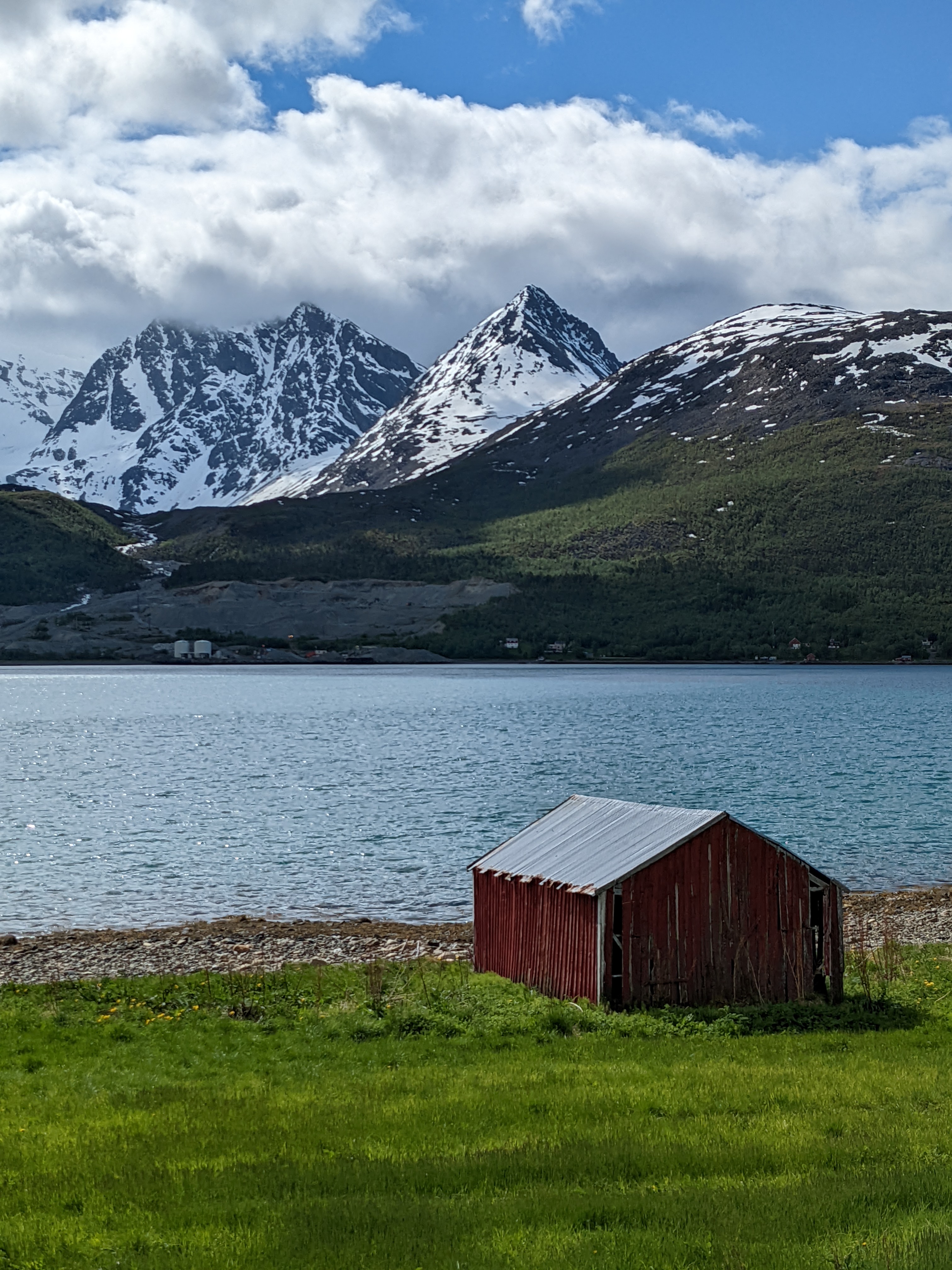 a red shed with fjord and mountains behind - also, an industrial site in the distance