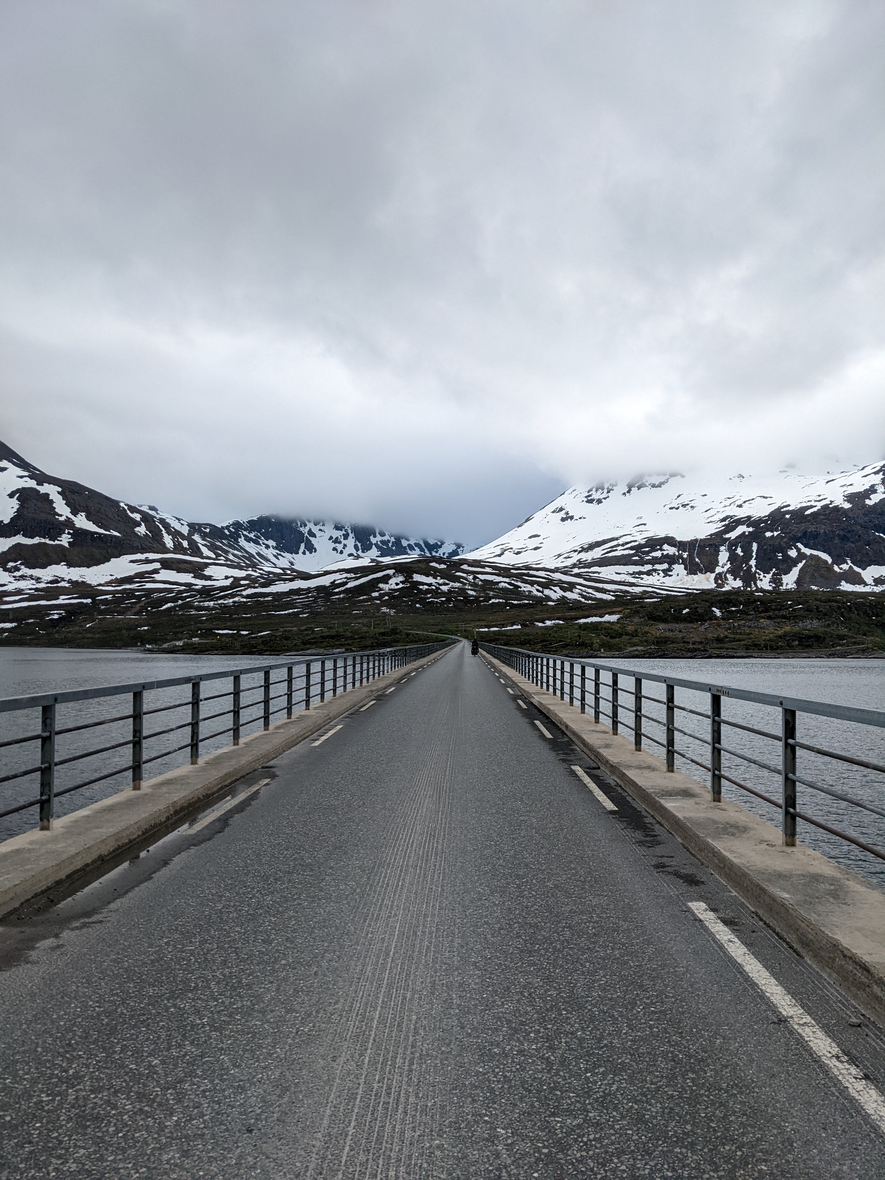 H rides across the bridge off of Skervøy with snowy mountains in the background